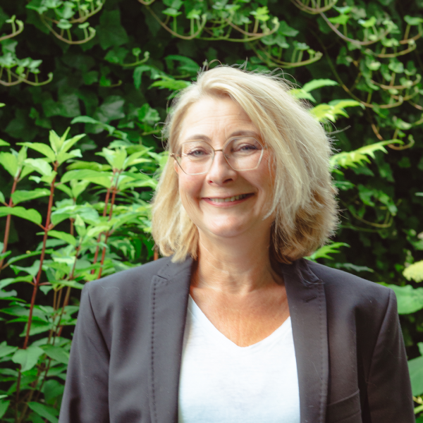 Margret met wit shirt en zwarte jas in de tuin